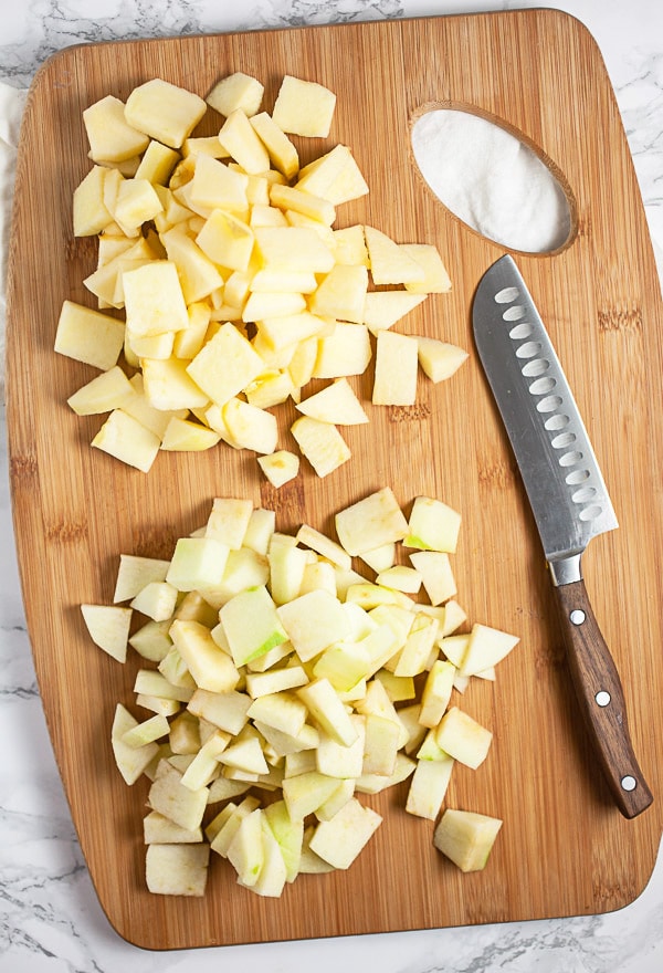 Peeled and diced Granny Smith and Fuji apples on wooden cutting board with knife.