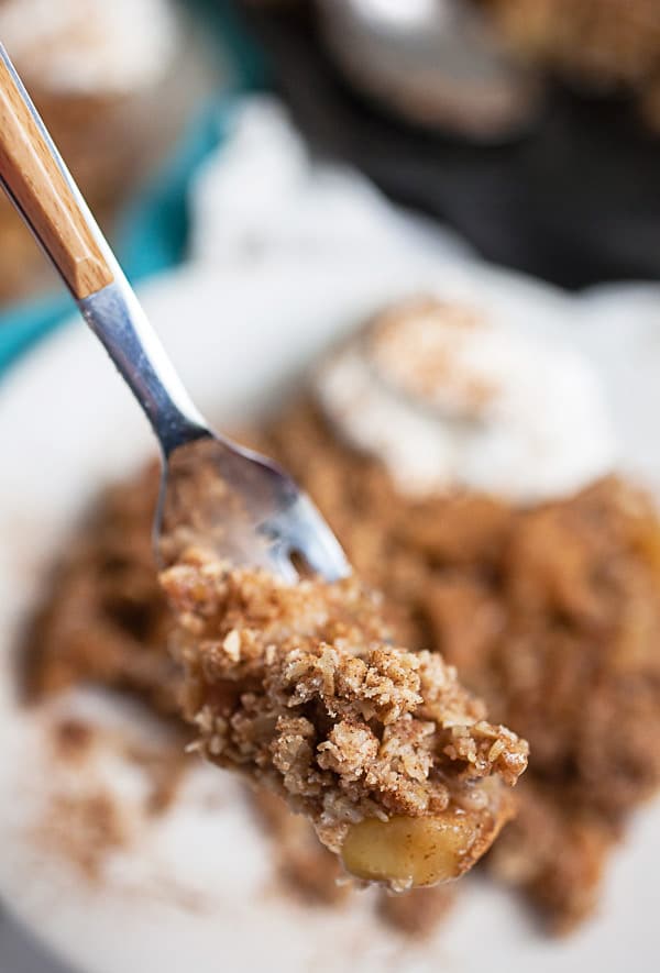 Bite of apple crisp on fork lifted from small white plate.