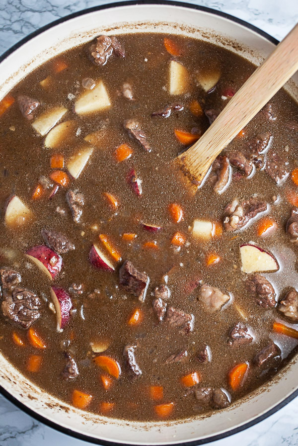 Uncooked beef stew with carrots, potatoes, and broth in cast iron Dutch oven.