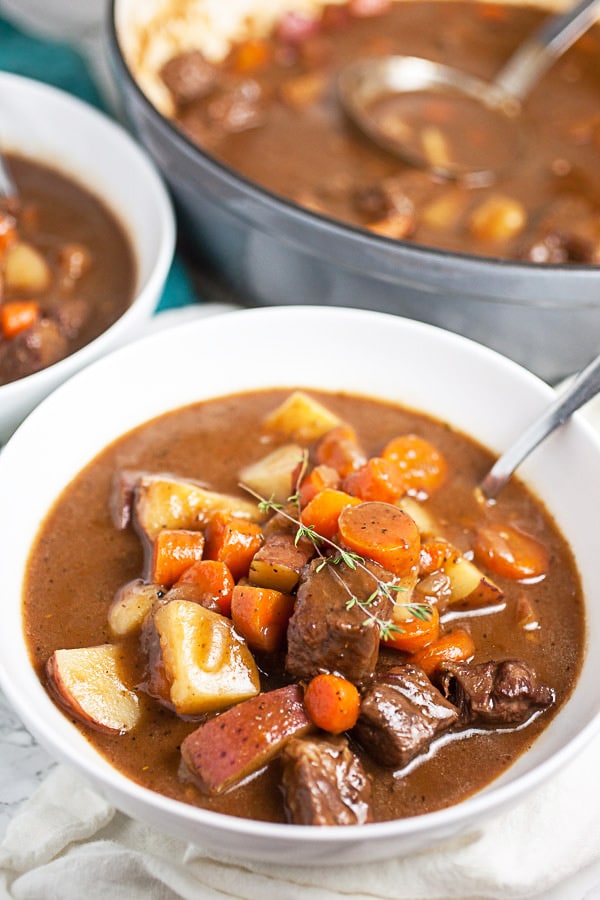 Beef stew in white bowls garnished with thyme next to Dutch oven.