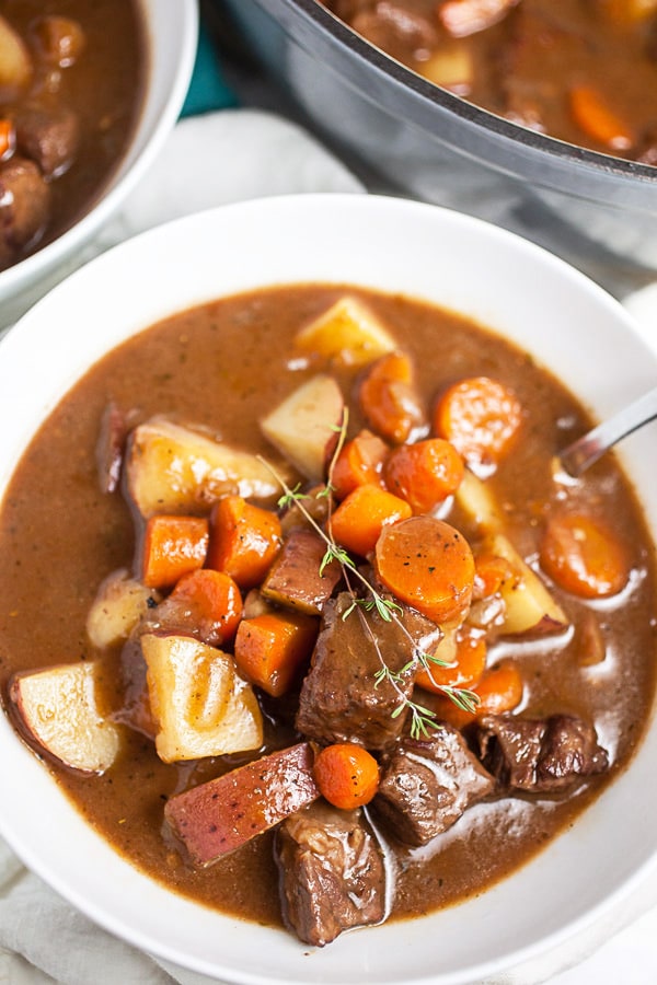 Gluten free beef stew in white bowl with spoon garnished with thyme.