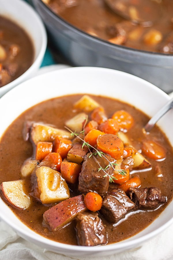 Beef stew in white bowl next to Dutch oven.