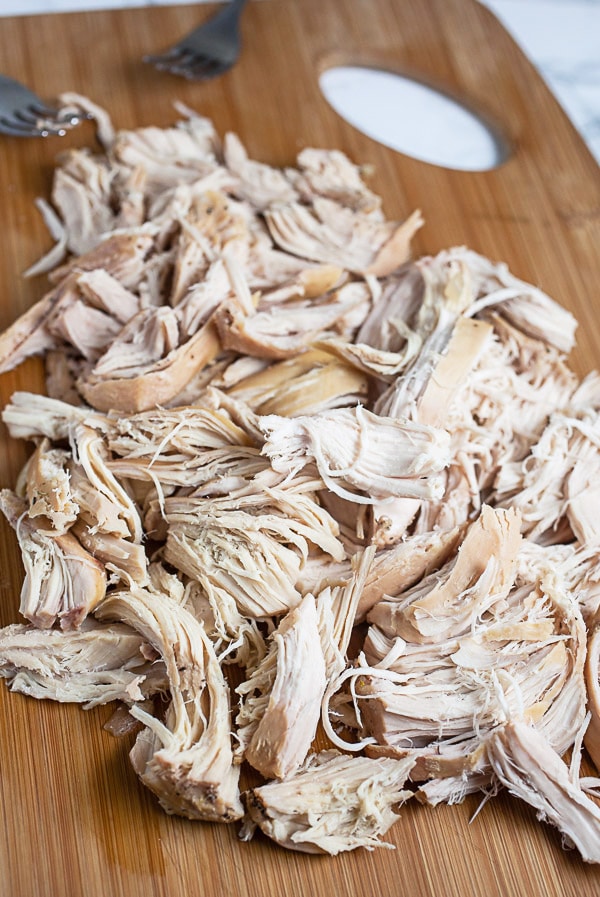Cooked shredded chicken on wooden cutting board.