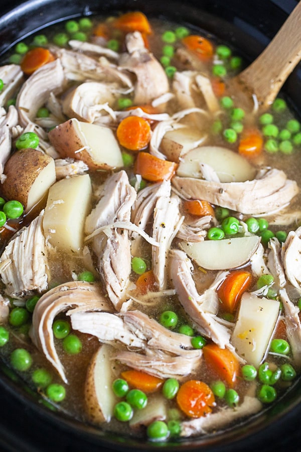 Cooked soup with shredded chicken, potatoes, carrots, and peas in crockpot.