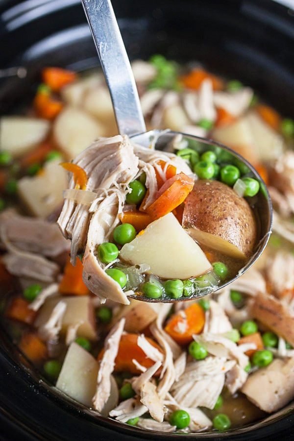 Scoop of chicken potato soup lifted from slow cooker using metal ladle.