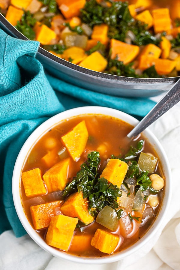 Sweet potato soup with kale in small white bowl next to Dutch oven.