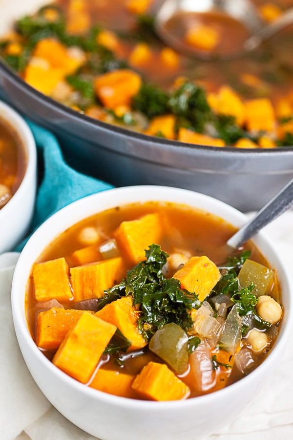 Sweet potato kale soup with chickpeas in small white bowl next to Dutch oven.
