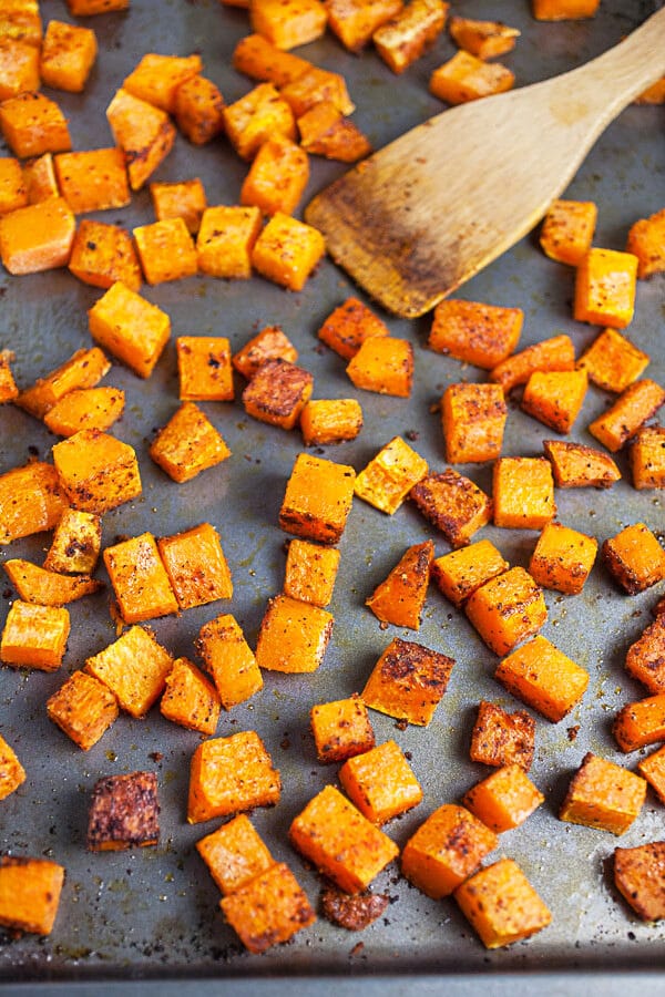 Roasted butternut squash on metal baking sheet with wooden spatula.