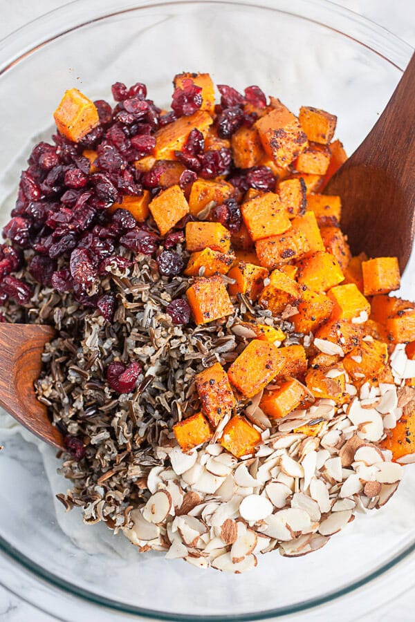 Wild rice, butternut squash, dried cranberries, and sliced almonds in large glass mixing bowl.