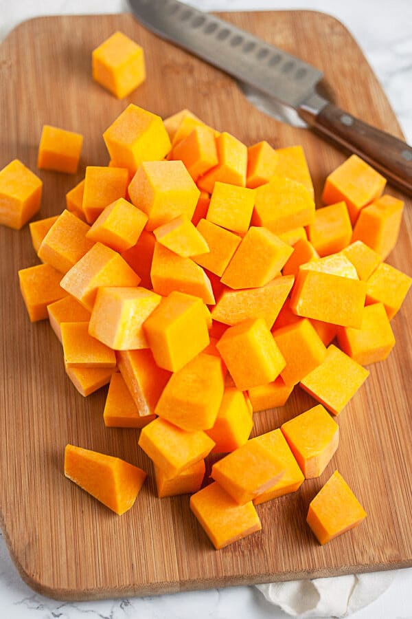Peeled and cubed butternut squash on wooden cutting board with knife.