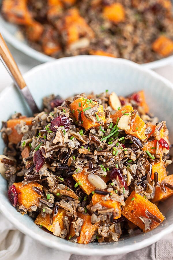 Wild rice salad with butternut squash, almonds, and cranberries in blue bowl with fork.