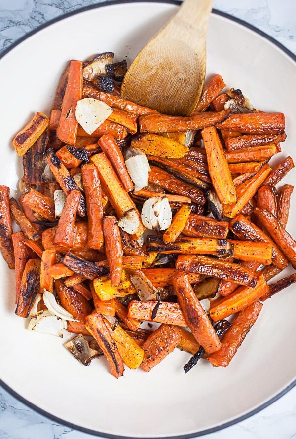 Roasted carrot slices, onions, and garlic cloves in white cast iron Dutch oven.