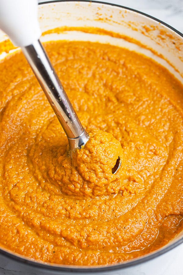 Carrot soup pureed with immersion blender in white cast iron Dutch oven.