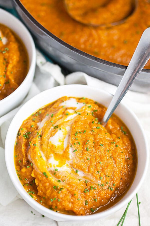 Roasted carrot soup in small white bowls next to Dutch oven.