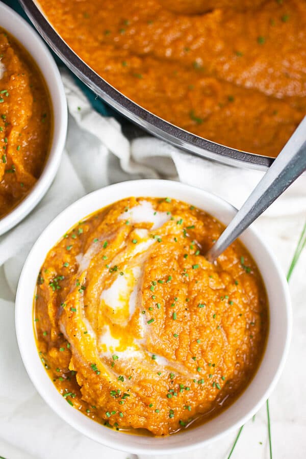 Roasted carrot soup in small white bowl with coconut milk and minced chives.