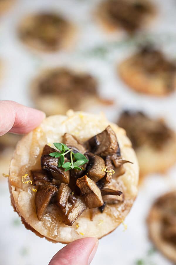 Fingers holding mushroom gruyere tartlet.