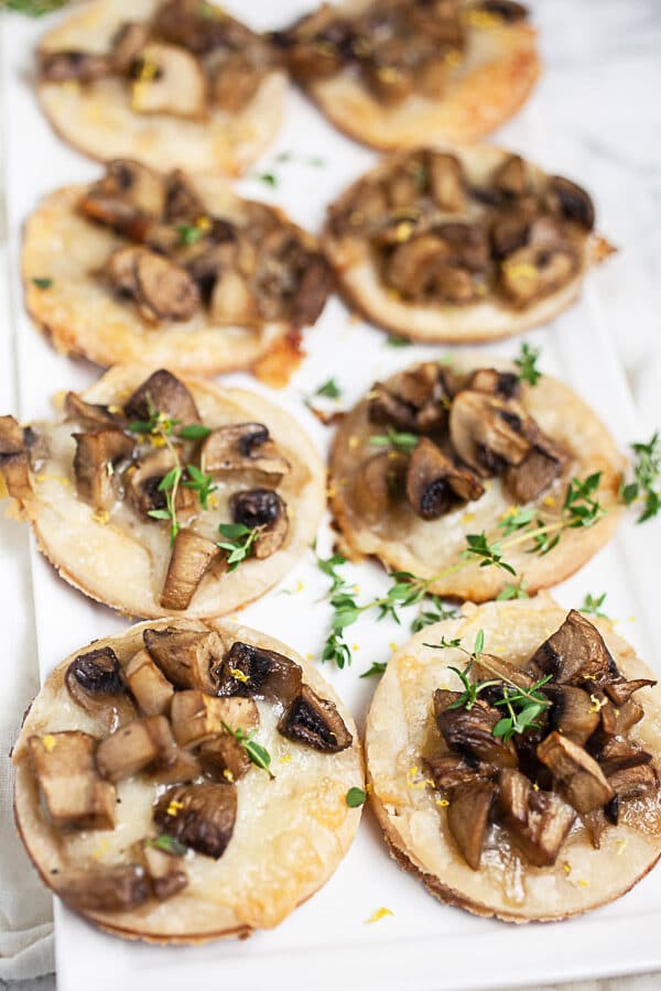 These Mushroom, Gruyere, and Thyme Tartlets are sure to be the hit of your party! This simple appetizer recipe is decadent and savory. Mushrooms and Gruyere cheese on Puff Pastry is the best flavor combination. These tarts are great for holiday parties or any get-together! #tartlets #tarts #mushroom #gruyere #appetizers #holidays Mushroom-Gruyere-Thyme-Tartlets-On-White-Serving-Platter