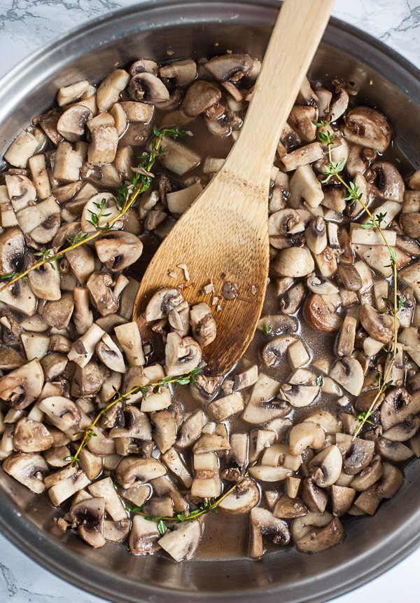 Mushrooms sautéed in skillet with wooden spoon. 