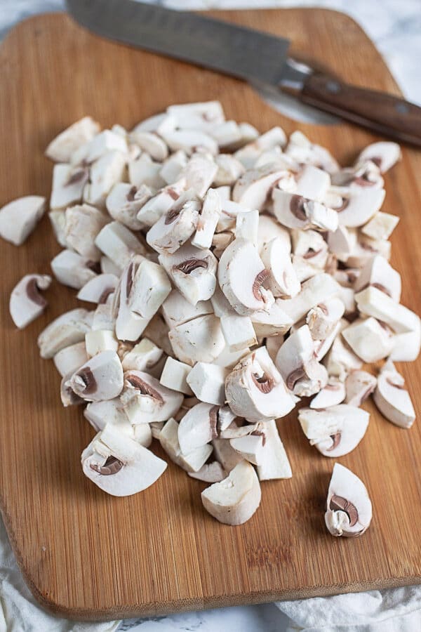 Chopped mushrooms on wooden cutting board with knife.