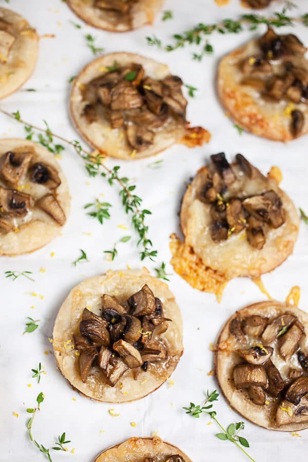 Mushroom gruyere tartlets garnished with fresh thyme on white surface.