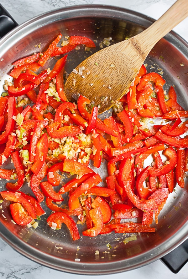 Red bell peppers sautéed with garlic in skillet.