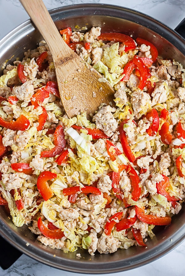 Cooked ground chicken, red bell peppers, and Napa cabbage in skillet.