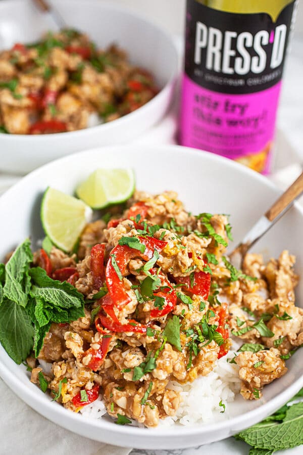 Ground chicken rice bowls with fresh mint and lime wedges in white bowl next to cooking oil.