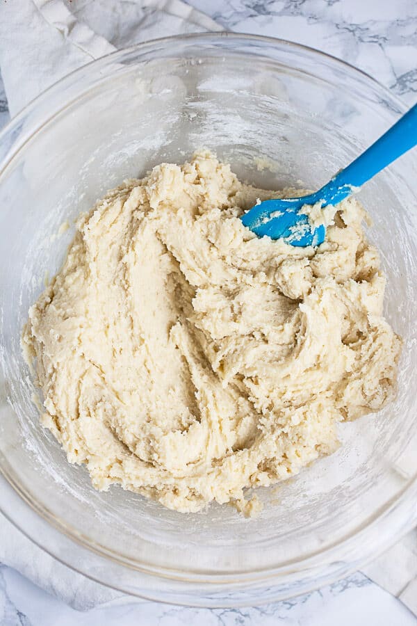 Sugar cookie dough in large glass mixing bowl with blue spatula.