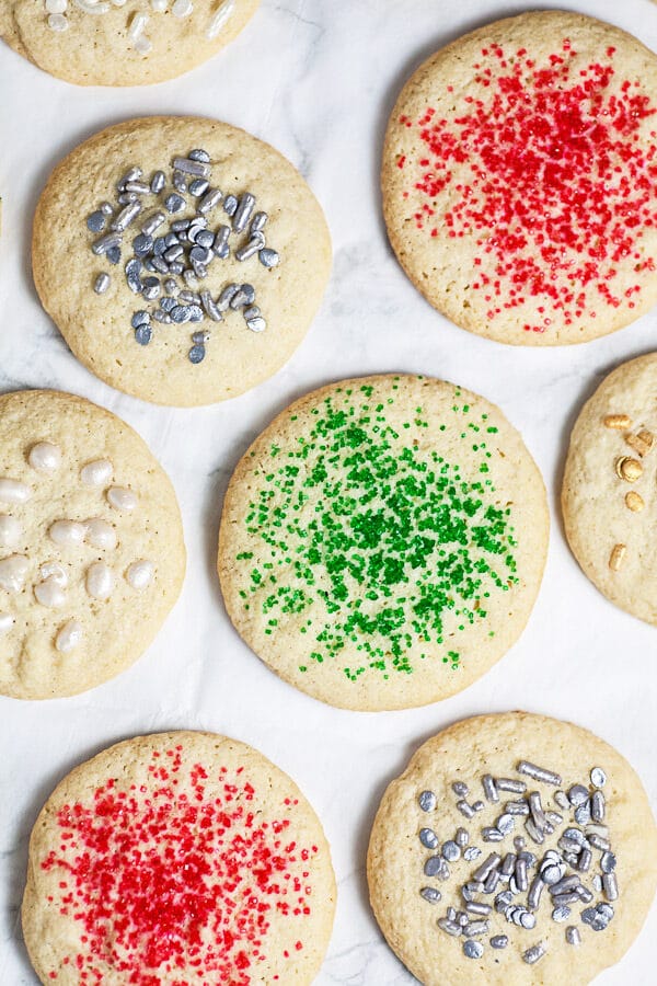 Baked sugar cookies with sprinkles on white surface.