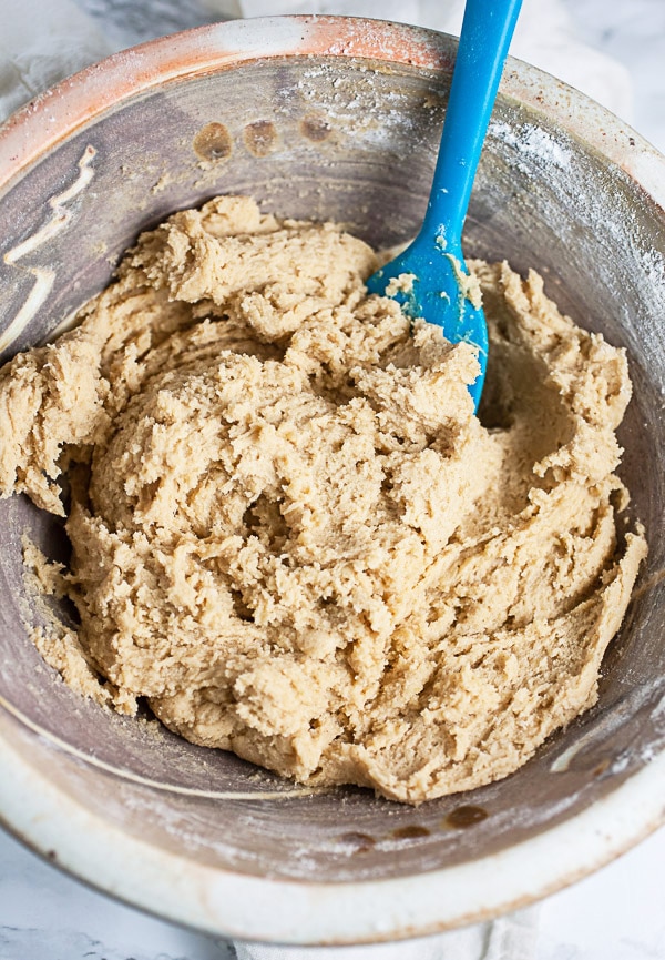 Peanut butter cookie dough batter in ceramic bowl with blue spatula.