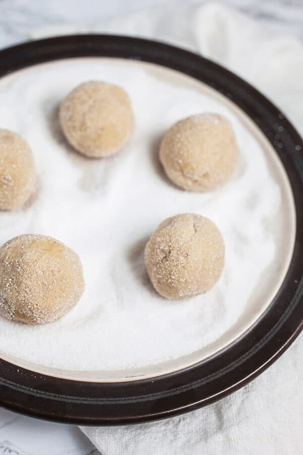 Unbaked cookie dough balls rolled in sugar on plate.