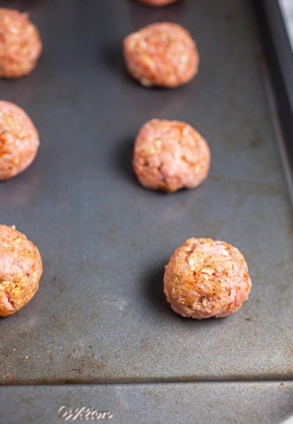 Uncooked turkey meatballs on metal baking sheet.