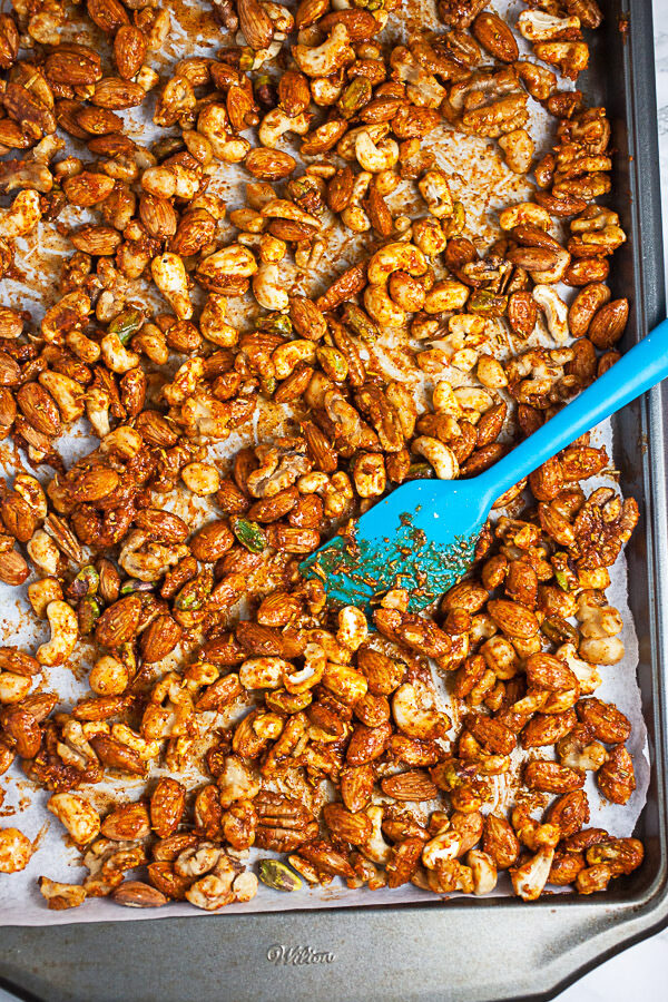 Uncooked nuts tossed in glaze on metal baking sheet.