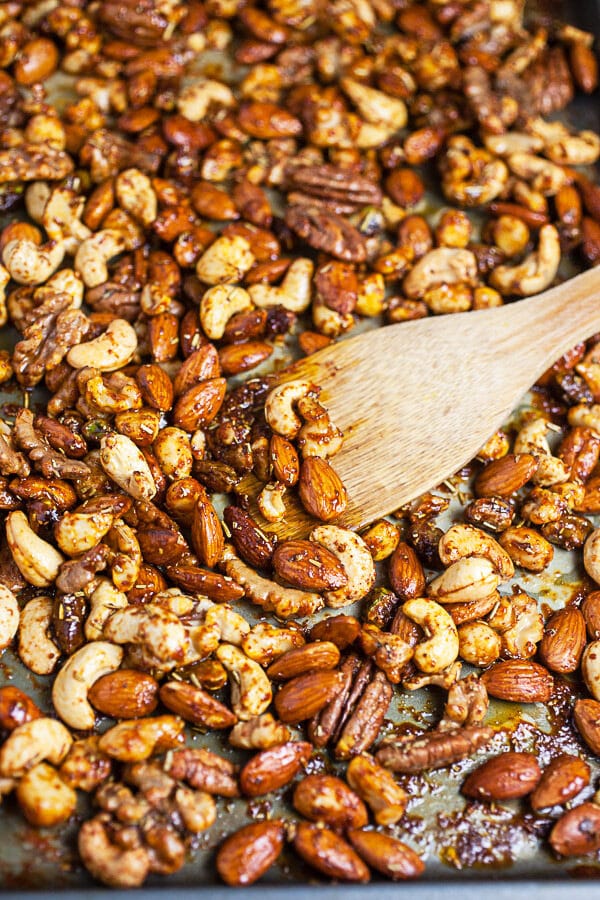 Cooked roasted mixed nuts on metal baking sheet with wooden spatula.