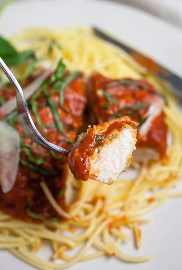 Bite of gluten free chicken parmesan on fork lifted from plate.