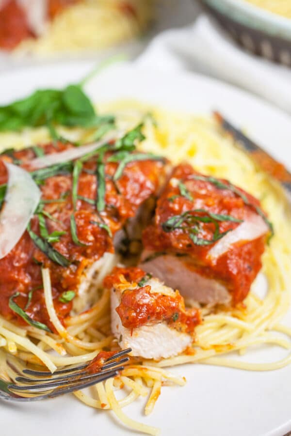 Chicken Parmesan in marinara sauce cut into pieces on top of spaghetti noodles.