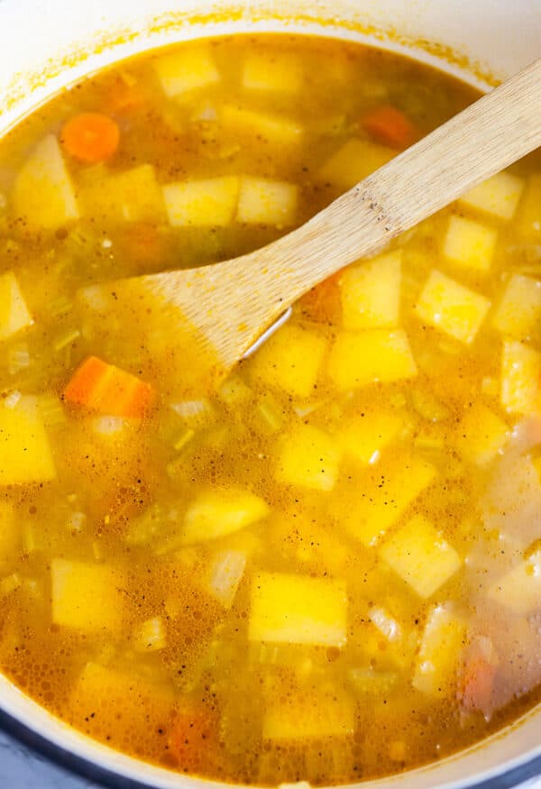 Uncooked vegetable soup in Dutch oven with wooden spoon.