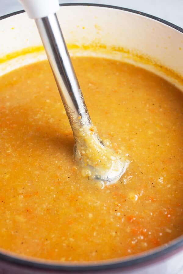 Immersion blender pureeing root vegetable soup in soup pot.