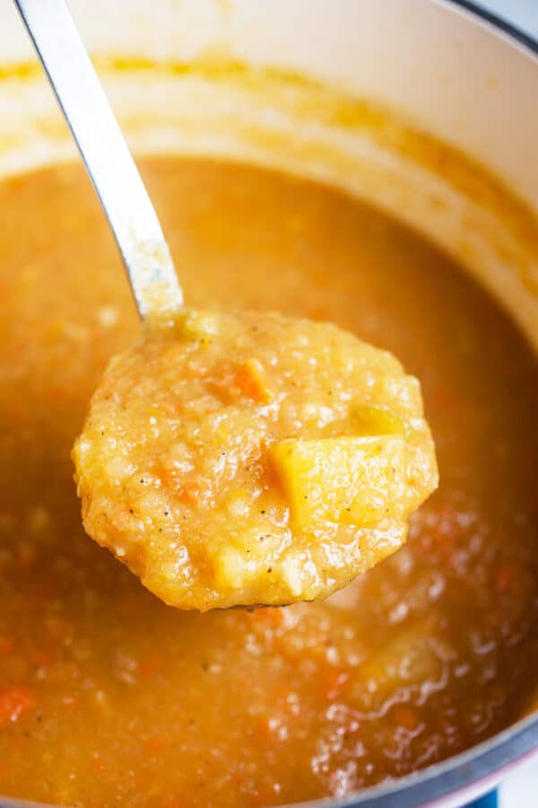 Scoop of pureed vegetable soup lifted from soup pot in metal ladle.