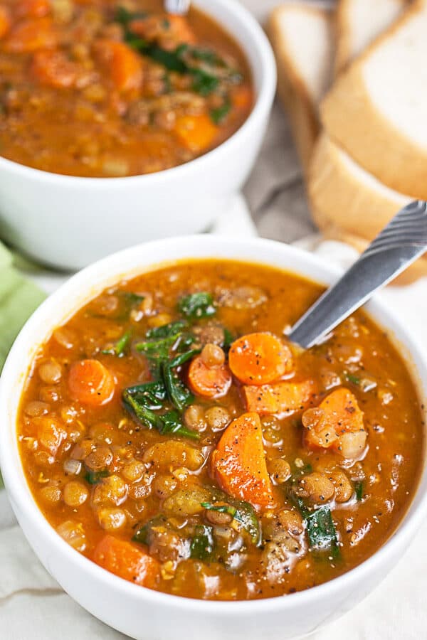 Lentil soup in white bowls next to bread.