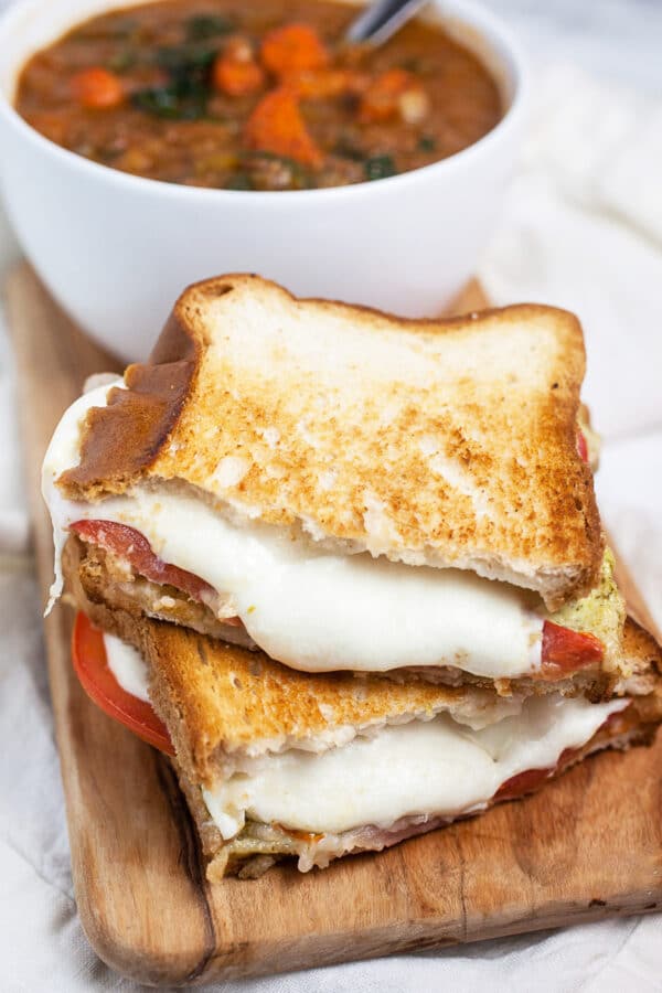 Italian mozzarella grilled cheese sandwich cut in half with small white bowl of soup.