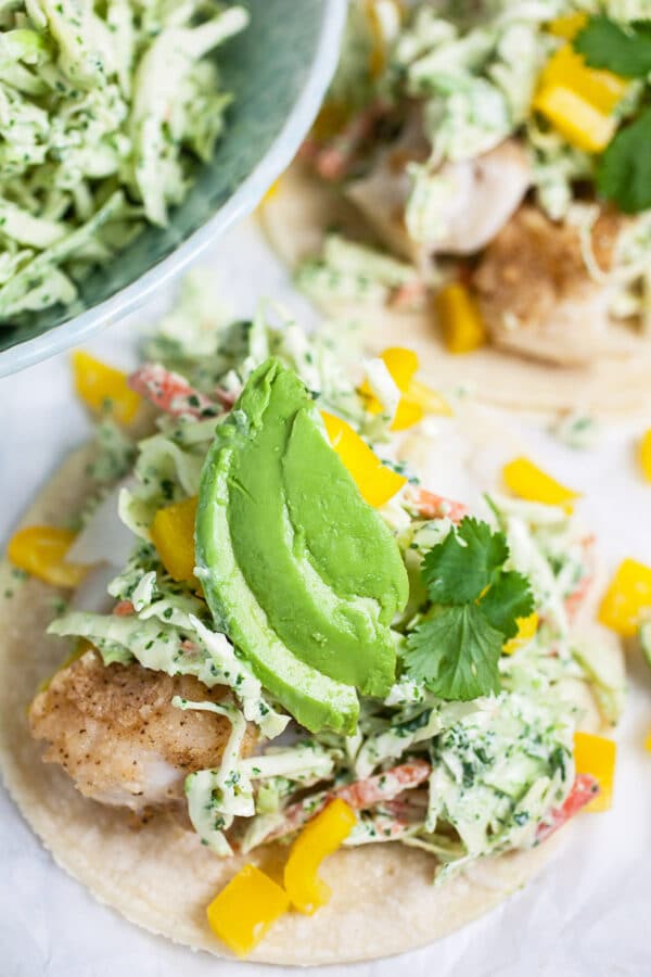 Fish tacos with cilantro lime slaw, peppers, avocado, and cilantro on corn tortillas.