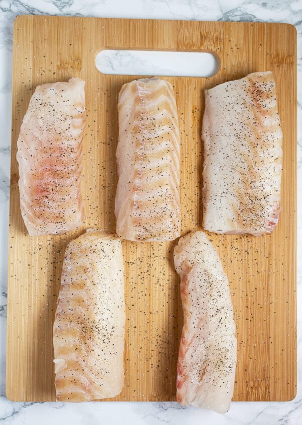 Sliced cod filets on wooden cutting board with salt and pepper.