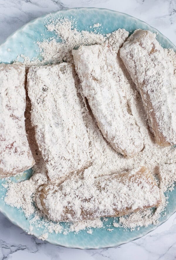 Uncooked fish filets in flour mixture in blue bowl.