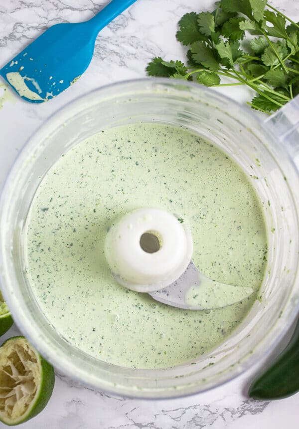 Cilantro lime coleslaw dressing in food processor with limes and fresh cilantro.