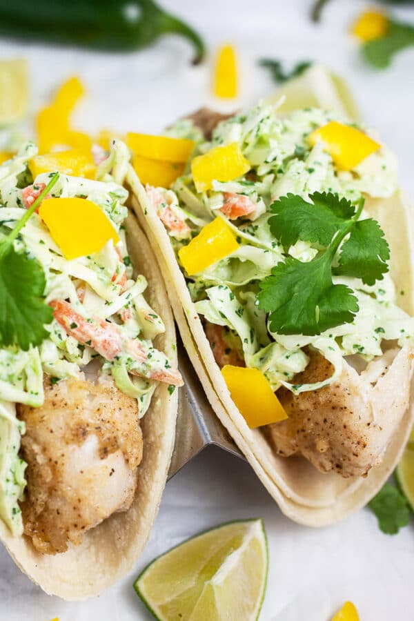 Fish tacos with cilantro lime slaw, bell peppers, cilantro, and lime wedges.