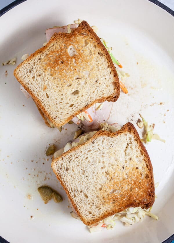 Rachel sandwiches toasting in white cast iron skillet.