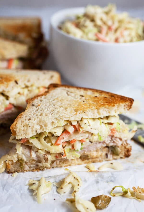 Rachel sandwich cut in half next to small white bowl of coleslaw.