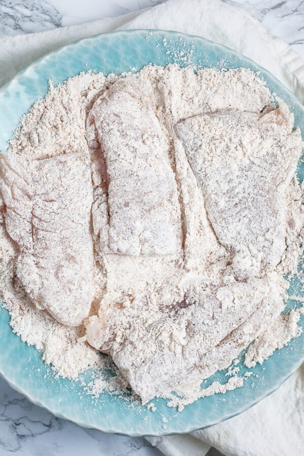 Walleye filets tossed in flour in blue bowl.