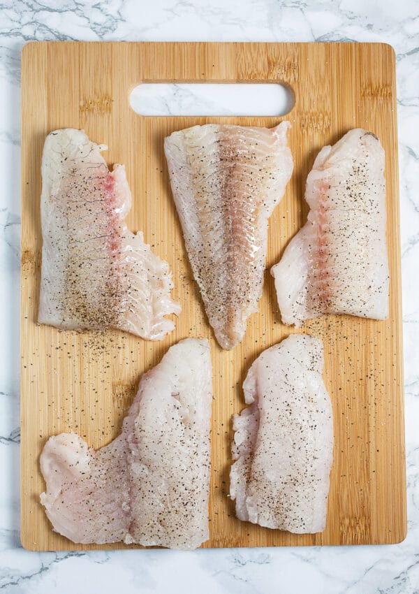 Walleye filets on wooden cutting board with salt and pepper.